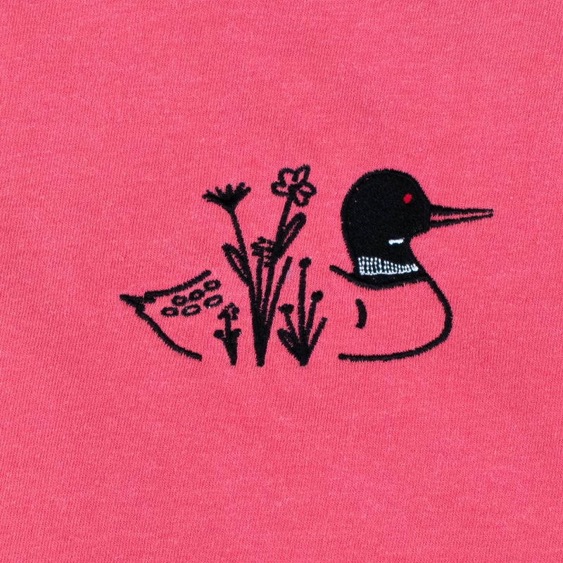 A close-up of a pink fabric surface featuring a black embroidered loon design with wildflowers on its body with a small red eye detail.